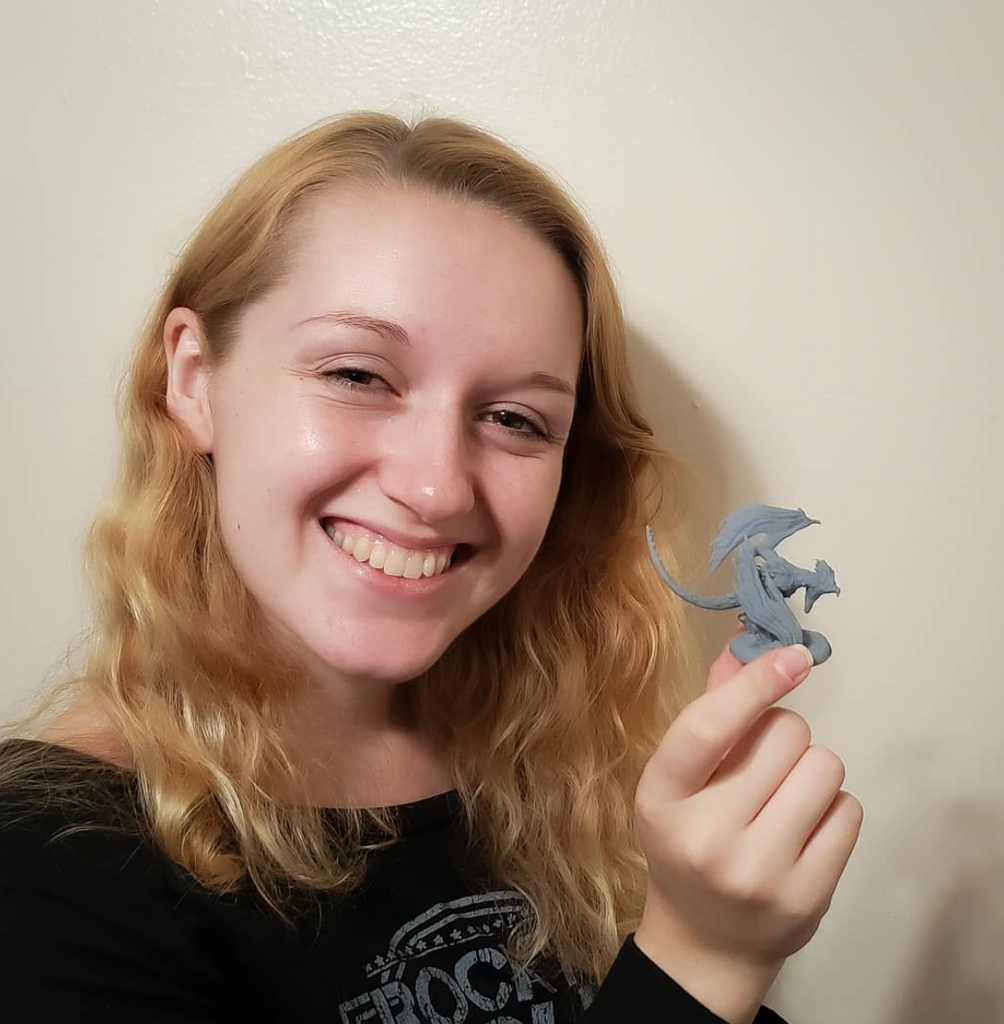 Image of Mia Kay, a 3D Designer, holding up a 3D printed design of a gray miniature dragon figurine.